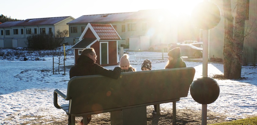 Några personer njuter av fjärrvärmen på lekplatsen i Sätra.